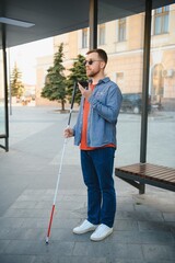 blind man with white cane waiting for public transport in city.