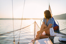 Stylish Female Tourist Resting On Yacht And Admiring Sunset Over Sea