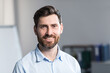 © Liubomir - Close up photo. Portrait of a young man in the office, office worker. With a beard in a light shirt. He looks at the camera, smiles