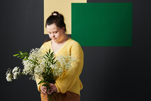Studio Portrait Of Modern Young Woman With Down Syndrome Wearing Stylish Casual Clothes Holding Bouquet Of White Flowers Looking At It
