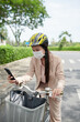 © DragonImages - Young female entrepreneur in medical mask checking smartphone on way to office