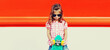 Portrait of stylish little girl child with skateboard in the city on red background