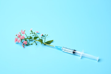 Syringe with pink flowers on blue background, beauty injections creative concept