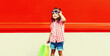 Little girl child with shopping bags in the city on red background