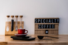 Coffee Cup On Table Near Glass Tubes With Beans And Letter Board