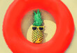 Summer vacation concept - pineapple and red inflatable ring on the beach sand background
