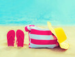 Summer vacation concept - bag with straw hat and flip flops on beach on blue sea background