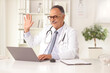 © Ljupco Smokovski - Mature male doctor sitting in an office and waving at a laptop computer