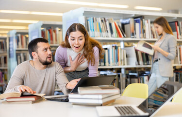 Canvas Print - Young guy and a girl students studying at the university, preparing for the exam in the library studying on a laptop ..and discussing something