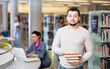 © JackF - Portrait of a confident student guy, standing in the university library, holding textbooks in his hands