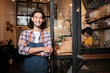 © tigercat_lpg - A long hair handsome Asian male startup barista with apron standing at casual cafe door, arms crossed, looking at the camera with and welcoming smile, happy and cheerful with coffee shop service jobs.