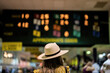 An attendee at a horse race, wearing a fancy hat in front of horse racing odds.