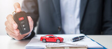 Businessman hand holding remote keyless with car toy, pen and contract document. buy and sale, insurance, rental and contract agreement concepts