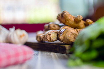 Whole raw fresh ginger place on a wooden chopping board surrounded by kitchen towel, whole garlic and herbs