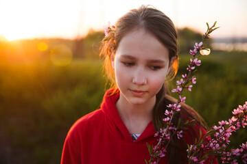 Wall Mural - Spring awakening. Slow life. Enjoying the little things. Dreaming of spring. thoughtful Preteen girl with a cherry blossom branch in the summer evening at sunset