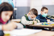 © dusanpetkovic1 - Profile of a pupil writing down schoolwork in notebook while sitting in classroom during covid 19.