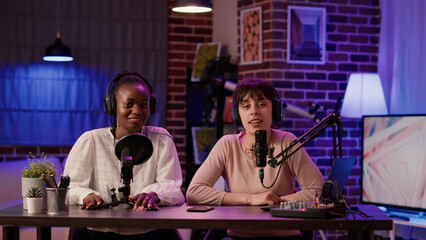 Two women recording dual vlog having casual conversation using professional microphone and audio mixer. Online podcast host talking with african american influencer creating digital content.