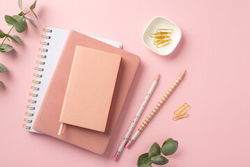 Business concept. Top view photo of workplace stack of pink planners pencils clips and eucalyptus on isolated pink background with blank space
