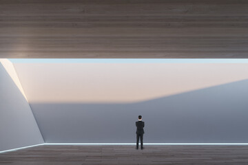 Poster - Thoughtful young businessman standing in abstract modern concrete and wooden interior with ceiling opening with sky view. Mock up place on walls.