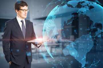 Poster - Attractive young caucasian businessman using laptop with glowing polygonal globe and social icons on blurry office interior background. Connect and data concept. Double exposure.