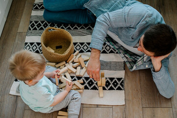 Happy father and toddler boy child little son playing with wooden blocks in children room at home