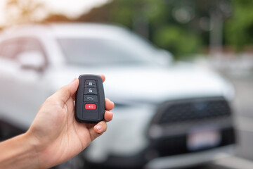 Hand holding car remote control, smart key to lock or unlock doors of white car. Safety, travel and transportation concept