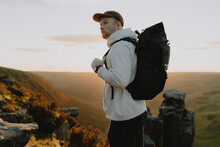 Male Hiker With Backpack On Top Of Mountain At Sunset, The Trinnacle, Derbyshire, England
