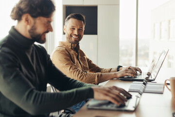 Poster - Happy male colleagues using laptops and communicating, working on business project together, discussing ideas in office