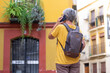 © luciano - Rear view of senior woman tourist in yellow t-shirt walking in the city street of Seville, Spain talking on mobile phone