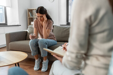 psychology, mental health and people concept - sad young woman patient with glass of water and woman psychologist at psychotherapy session