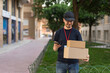 © Ezequiel Martínez - Repartidor mirando las cajas, con expresión feliz, en el jardín con el móvil. Fotografía horizontal con espacio para texto.