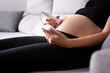 Pregnant woman with a fetal doppler listening to the baby's heart sitting on the sofa at home