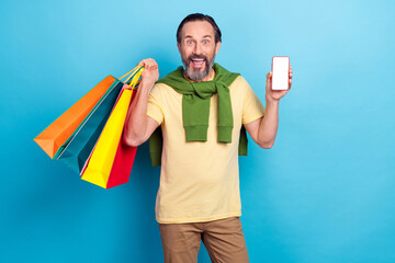 Poster - Photo of funky cheerful man demonstrate empty space display hold packages isolated on blue color background