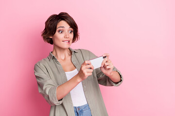 Poster - Portrait of positive funky girl hold device playing games biting lip isolated on pink color background