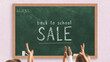 © Hakan - Back to school sale writing on green chalkboard, discount idea, marketing banner, students raising hands in front of the chalk board with wooden frame, school and classroom concept