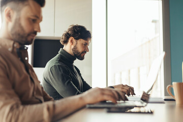 Poster - Focused male colleagues working on laptop computers at modern office, empty space