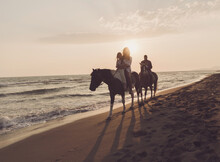The Family Spends Time With Their Children While Riding Horses Together On A Beautiful Sandy Beach On Sunet. 