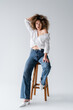 Trendy model in blouse sitting on chair on white background.