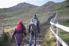Couple With Backpacks Hiking Up Stairs On Cliff