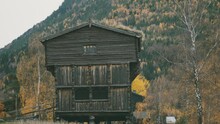 An Old Wooden House In The Norwegian Skansen. Autumn Forest Covers Mountain Slopes In The Background. Slow-motion, Pan Forward And Right.