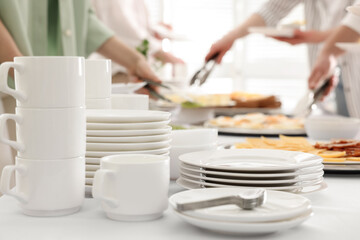 People taking food during breakfast, focus on clean dishware. Buffet service