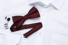 Stylish Burgundy Bow Tie And Cufflinks On White Shirt, Top View