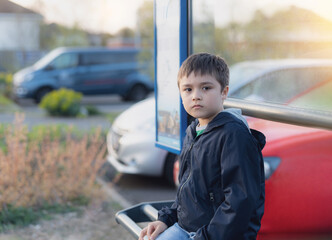 Wall Mural - Kid sitting at bus stop waiting for School bus.Portrait young boy looking at camera with thinking face, School child sitting outdoor bus station on sunny day spring or Summer