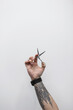 © alones - Cool man with a tattoo on his arm is holding a pair of scissors. The guy is a professional barber