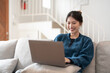 © Natee Meepian - Happy casual beautiful young asian woman working on a laptop sitting on the couch in the house.
