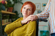 © pressmaster - Portrait of elderly woman with red hair looking at camera while sitting in wheelchair and holding hands with nurse standing behind