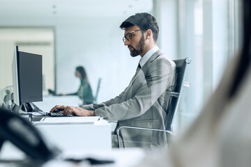 Handsome young entrepreneur working with computer while reading some documents in modern startup office.