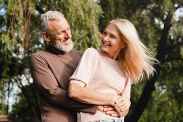 Wall Mural - Heterosexual couple. Caucasian mature spouses hugging embracing together in city park on romantic date. Love and relationship concept.