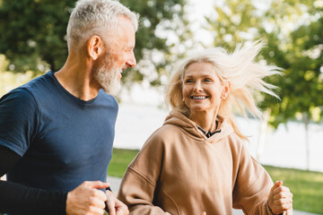 Mature middle aged senior couple running together in the park stadium looking at each other while jogging slimming exercises. Training workout