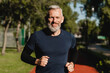 © InsideCreativeHouse - Cropped closeup portrait of a male mature athlete sportsman runner jogging in the morning in public park. Slimming exercises, active seniors concept.